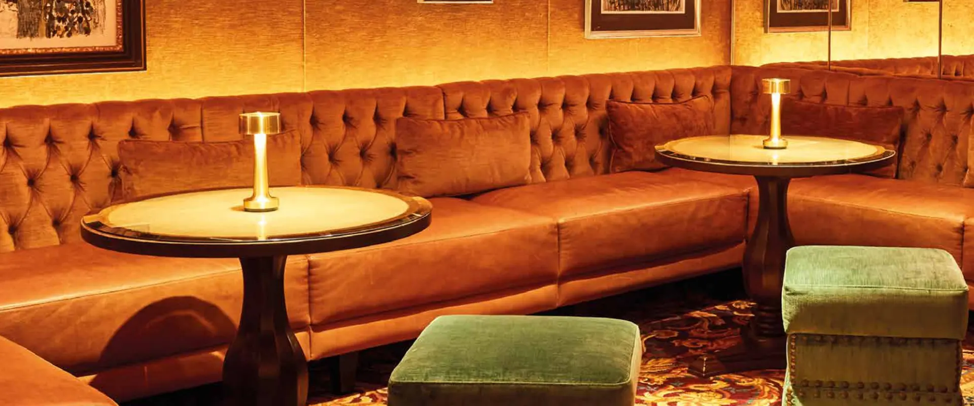 Eine gemütliche Sitzecke in der Jahreszeiten Bar mit einem großen, braunen Ledersofa, kleinen Beistelltischen und gedämpftem Licht.