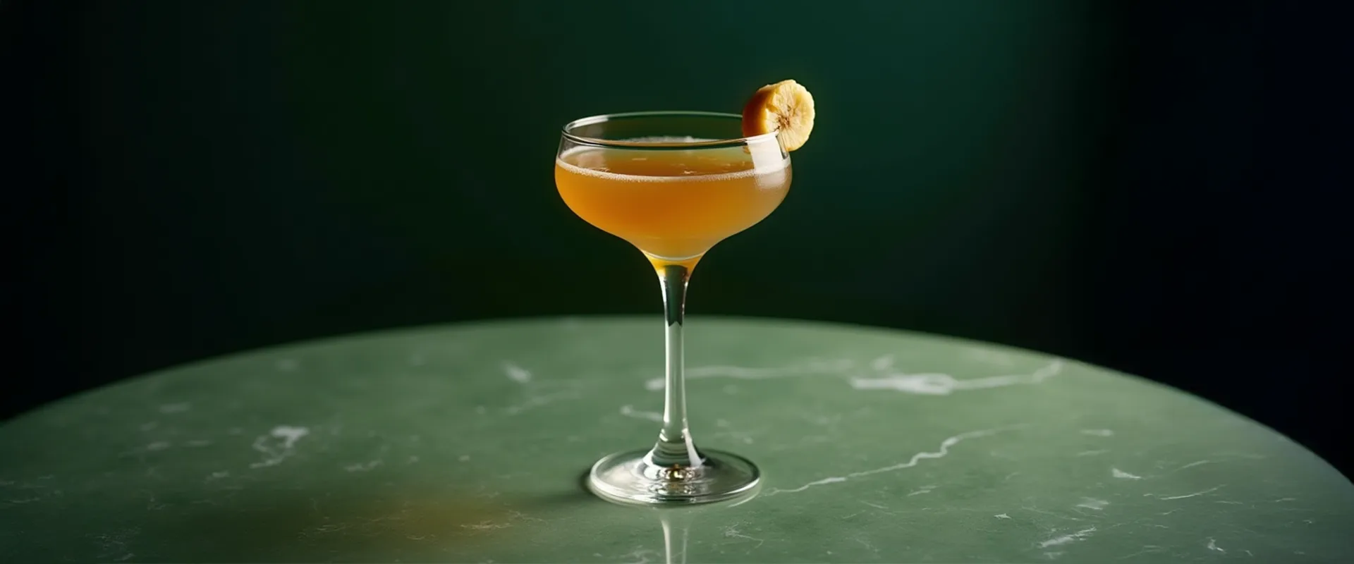 Platzhalter_1920x800 Ein Cocktailglas mit einem Cold brew banana tea steht auf einem Tisch, beleuchtet von natürlichem Licht. Das Glas ist mit einer Bananenscheibe garniert.