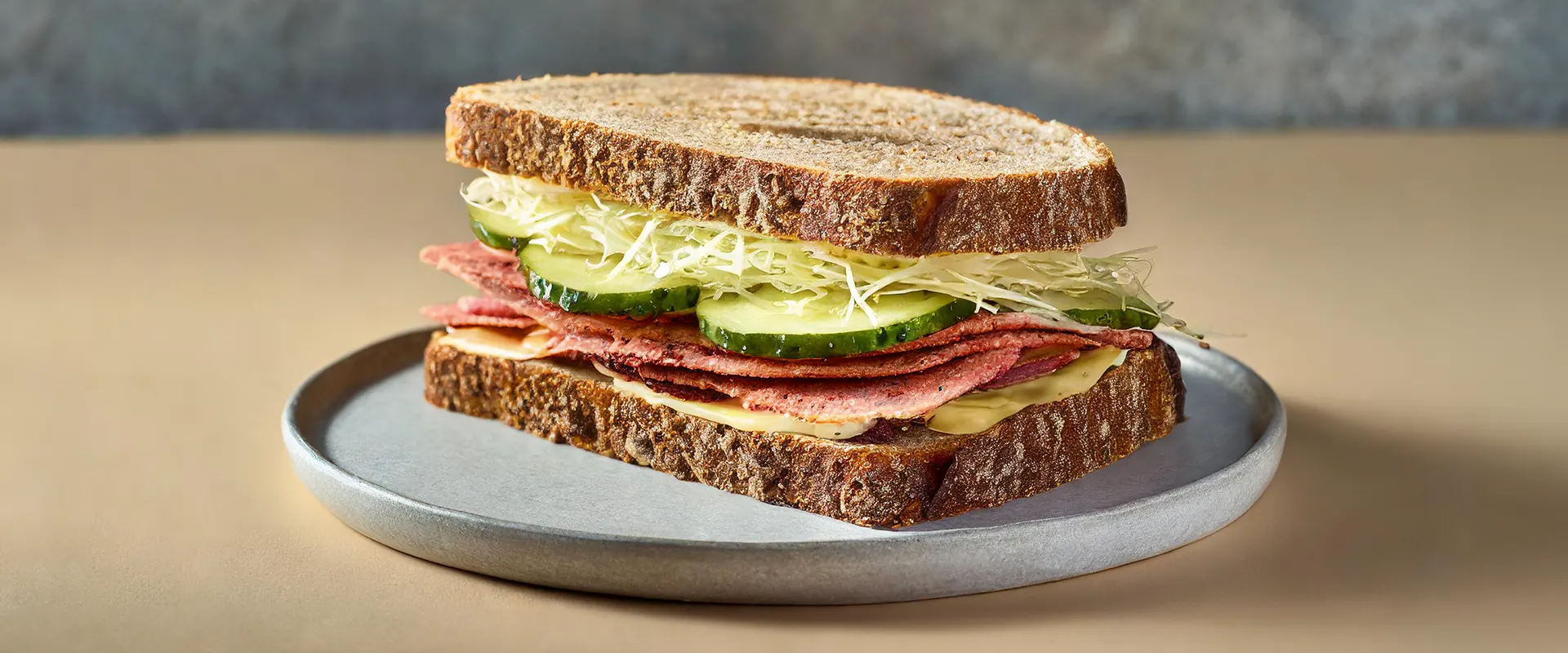 Platzhalter_1920x800 Ein saftiges Pastrami-Sandwich auf einem Teller, belegt mit Sauerkraut und Gurkenscheiben.