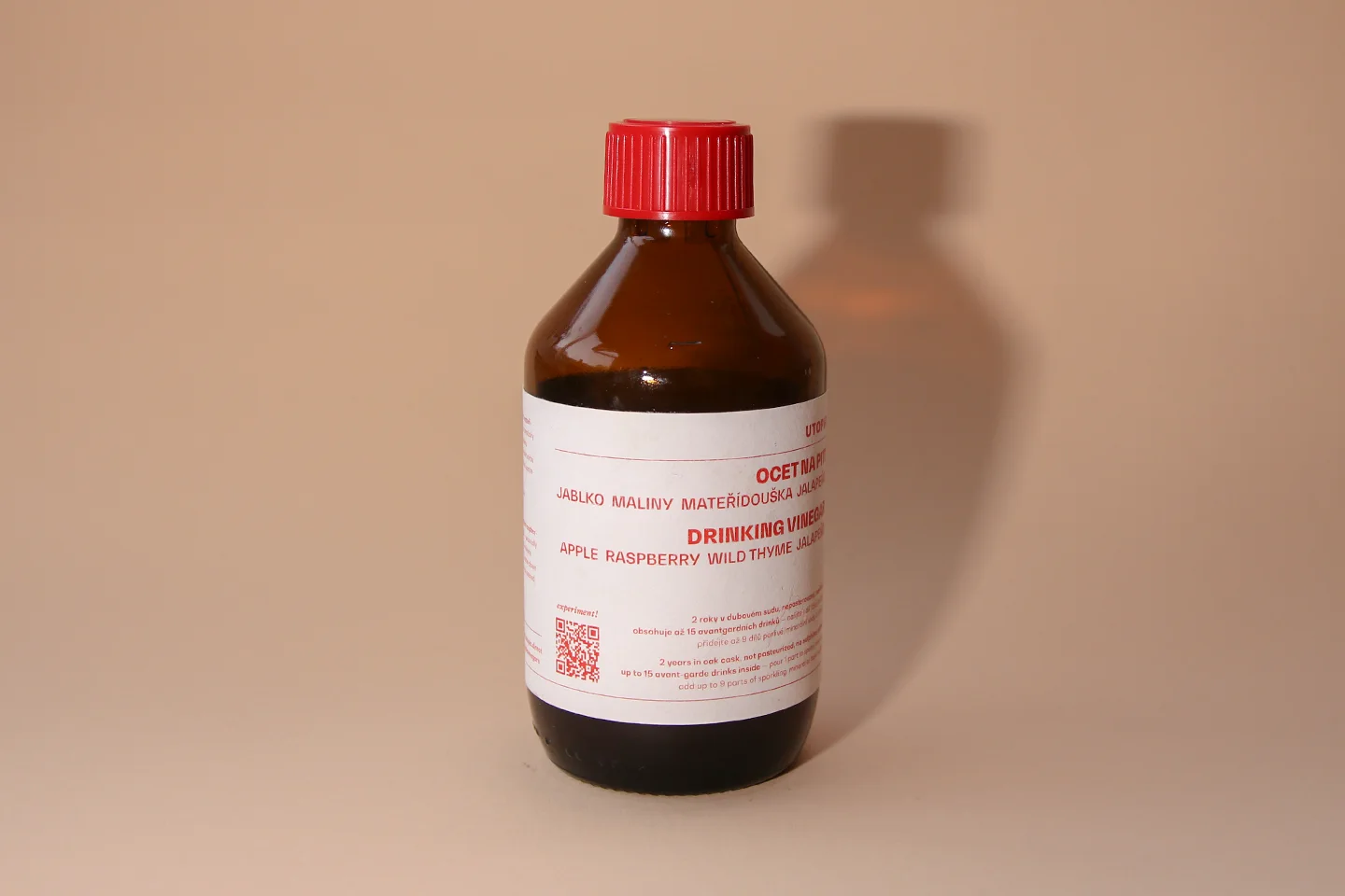 Braune Glasflasche mit rotem Deckel, gefüllt mit einem dunklen Apfel-Himbeer-Essig.